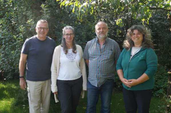 Die vier Vorstandsmitglieder stehen lächelnd und in sommerlicher Kleidung in einem Garten auf dem Rasen und im Hintergrund sind grüne Bäume und Hecken zu sehen.